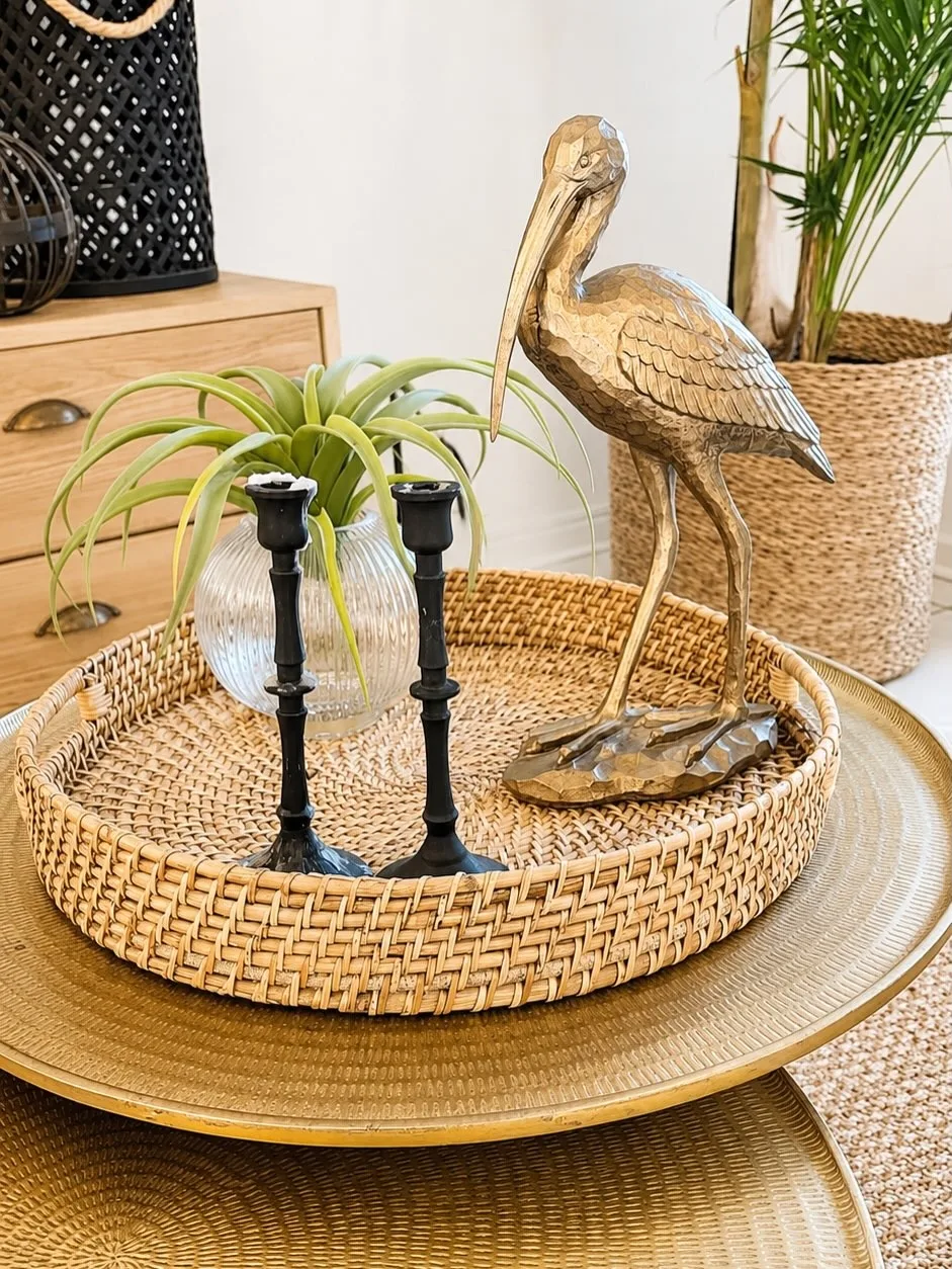 Pence House detail — a brass heron sculpture and black candlesticks on a woven rattan tray, styled with an air plant and brass platters
